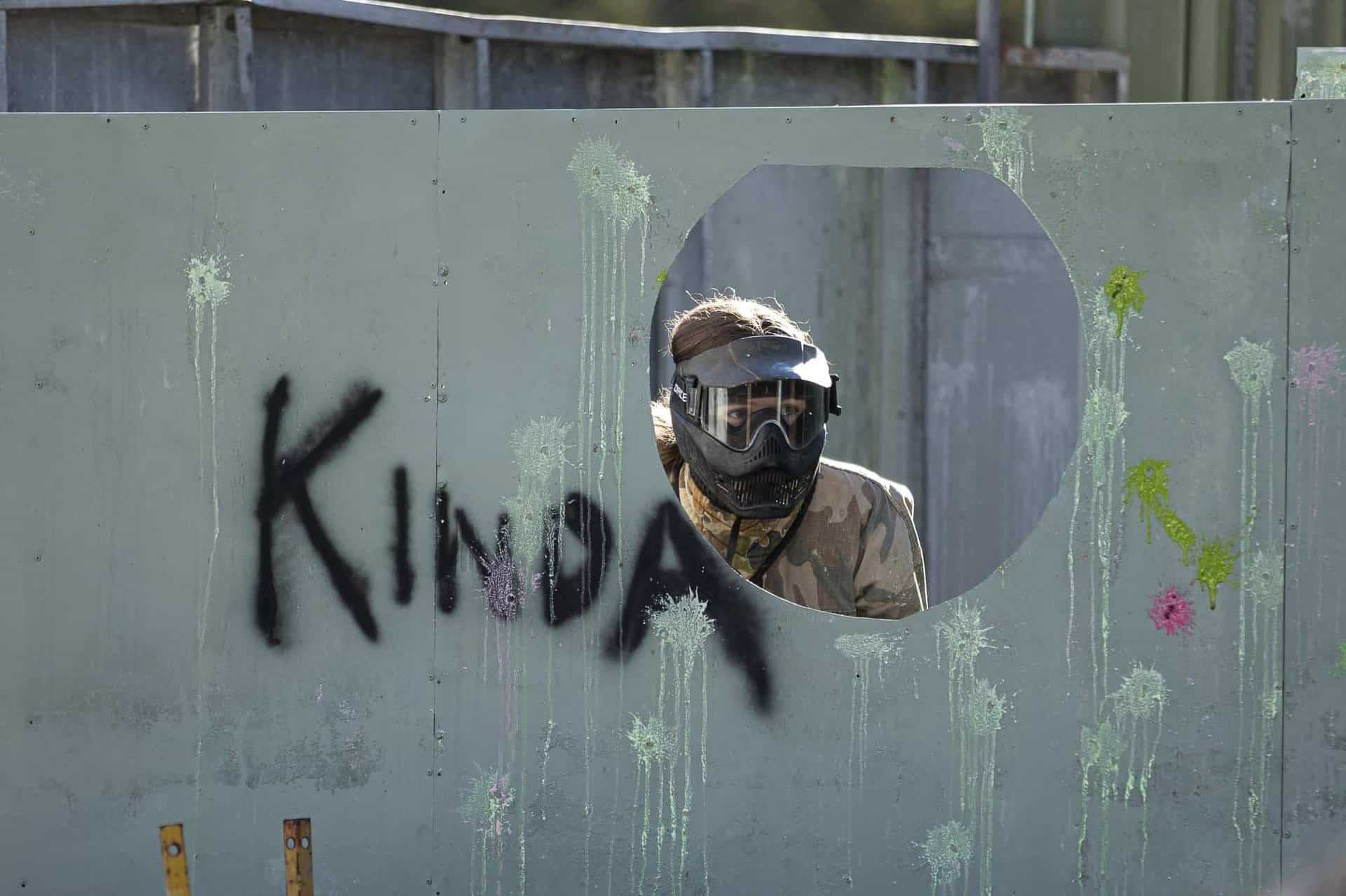 Girl hiding behind obstacle with her head poking out of a hole in paintball game