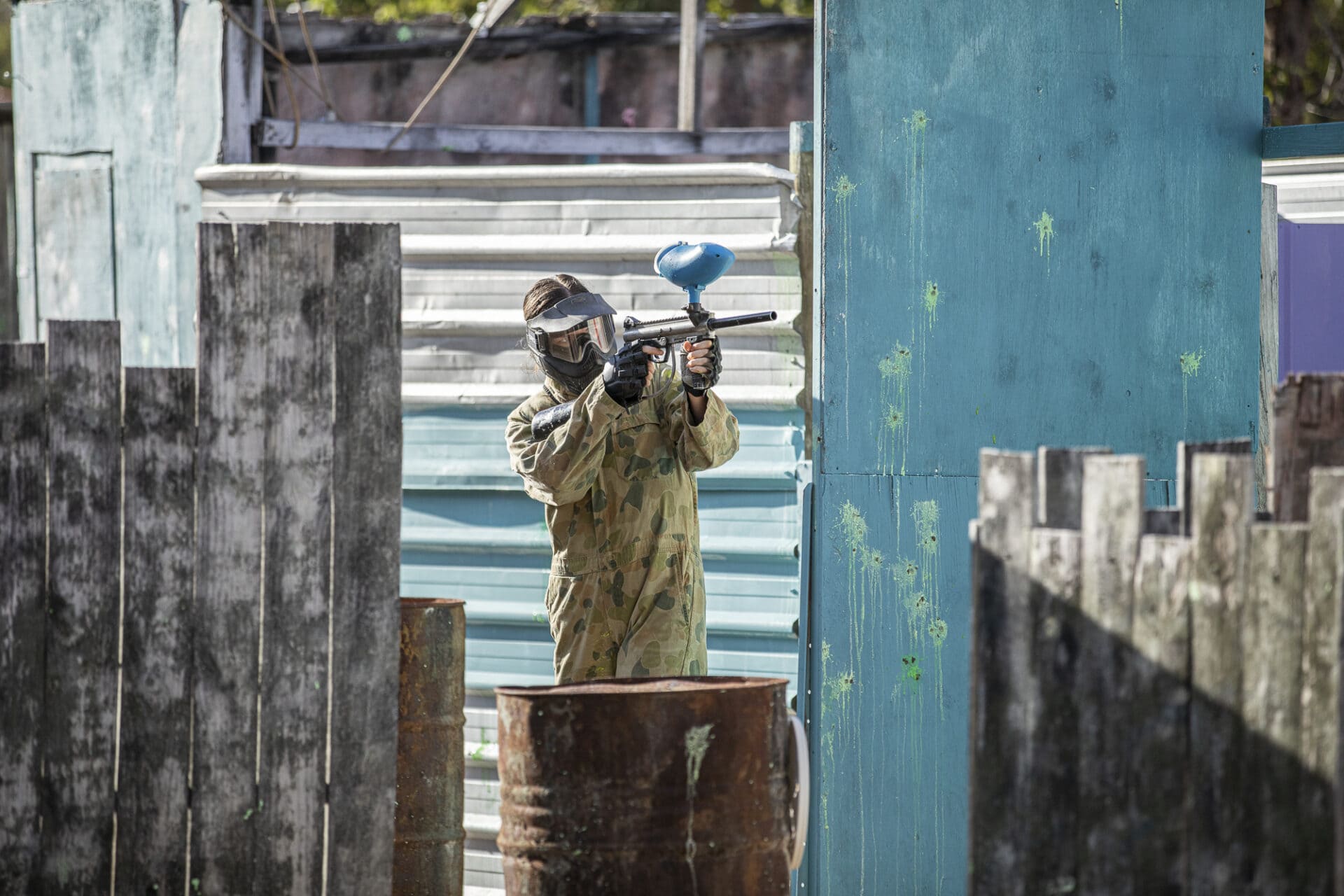 Paintball player firing from behind a barrel