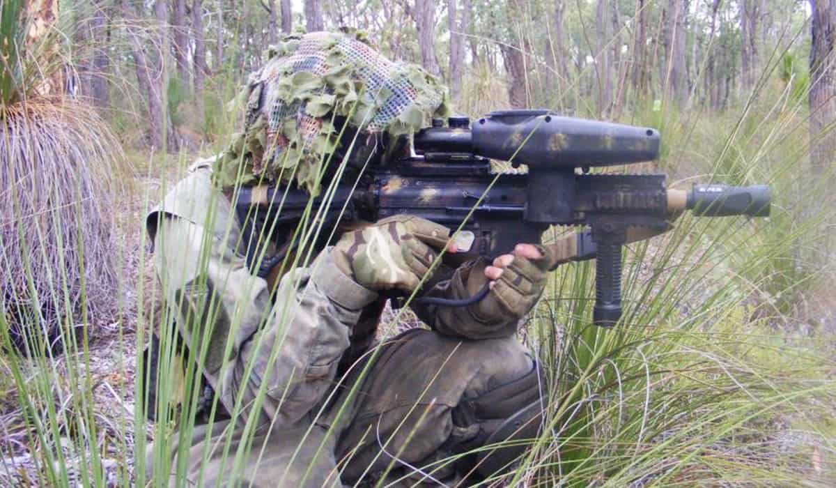A paintball player crouching down with camouflage like a sniper