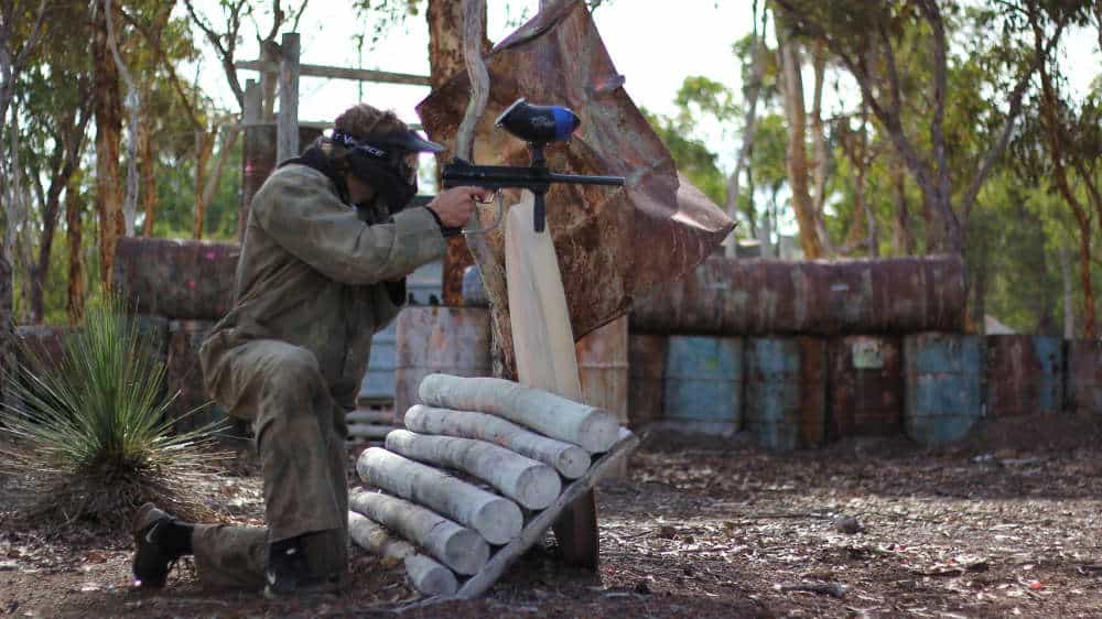 Paintball player taking aim from behind a pine barricade